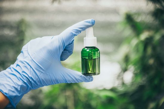 cbd-hemp-oil-hand-holding-bottle-of-cannabis-oil-against-marijuana-plant-6.jpg